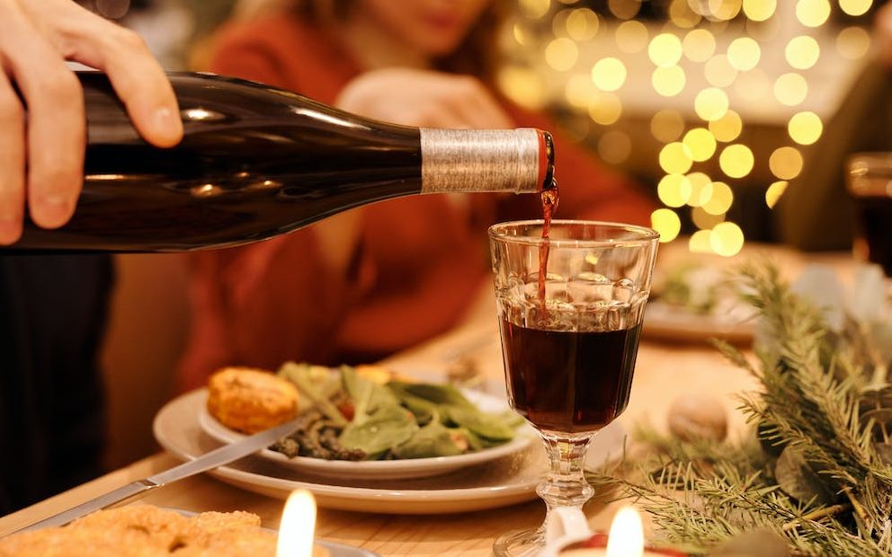 Person Pouring Wine into a Clear Glass at Christmas Dinner